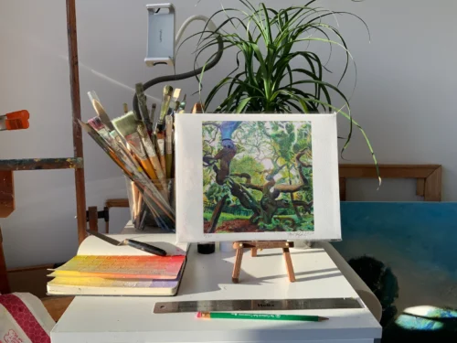 Print of Camperdown Elm artwork on an easel surrounded by artist's tools and plants in a sunlit studio.