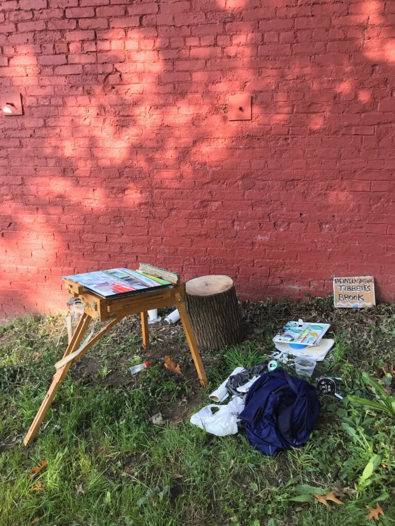 Artist's plein air setup at Siren Slope, with painting tools and a sign about Daylighting Tibbetts Brook.