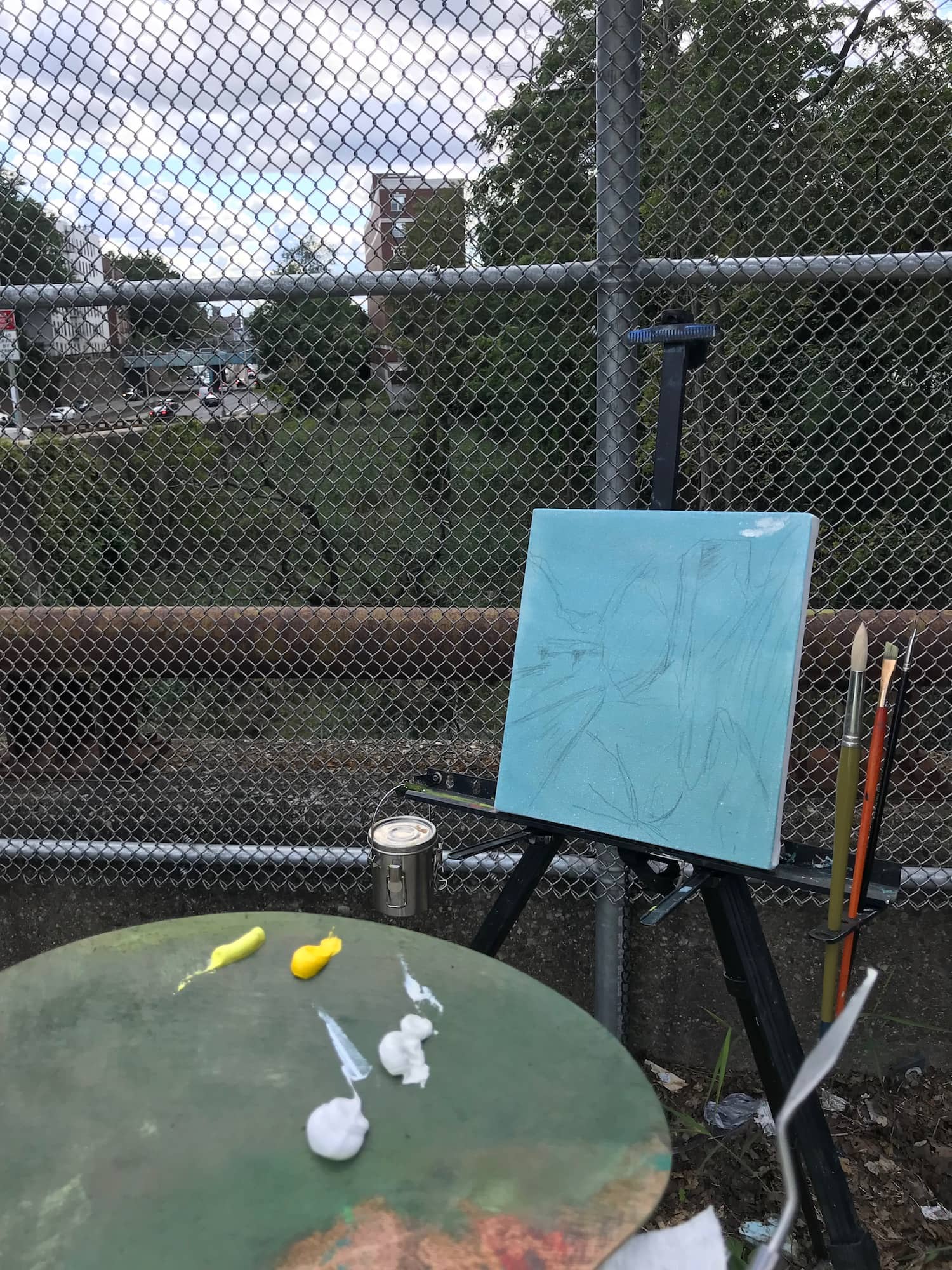 Artist's easel and palette with a preliminary blue canvas set against the backdrop of the CSX rail line and Major Deegan Expressway.