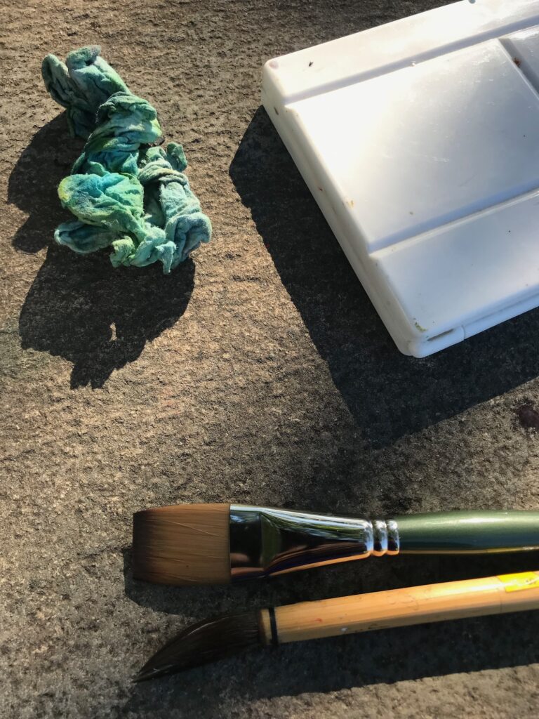 Painting brushes and a palette with blue and yellow paints rest on a table,