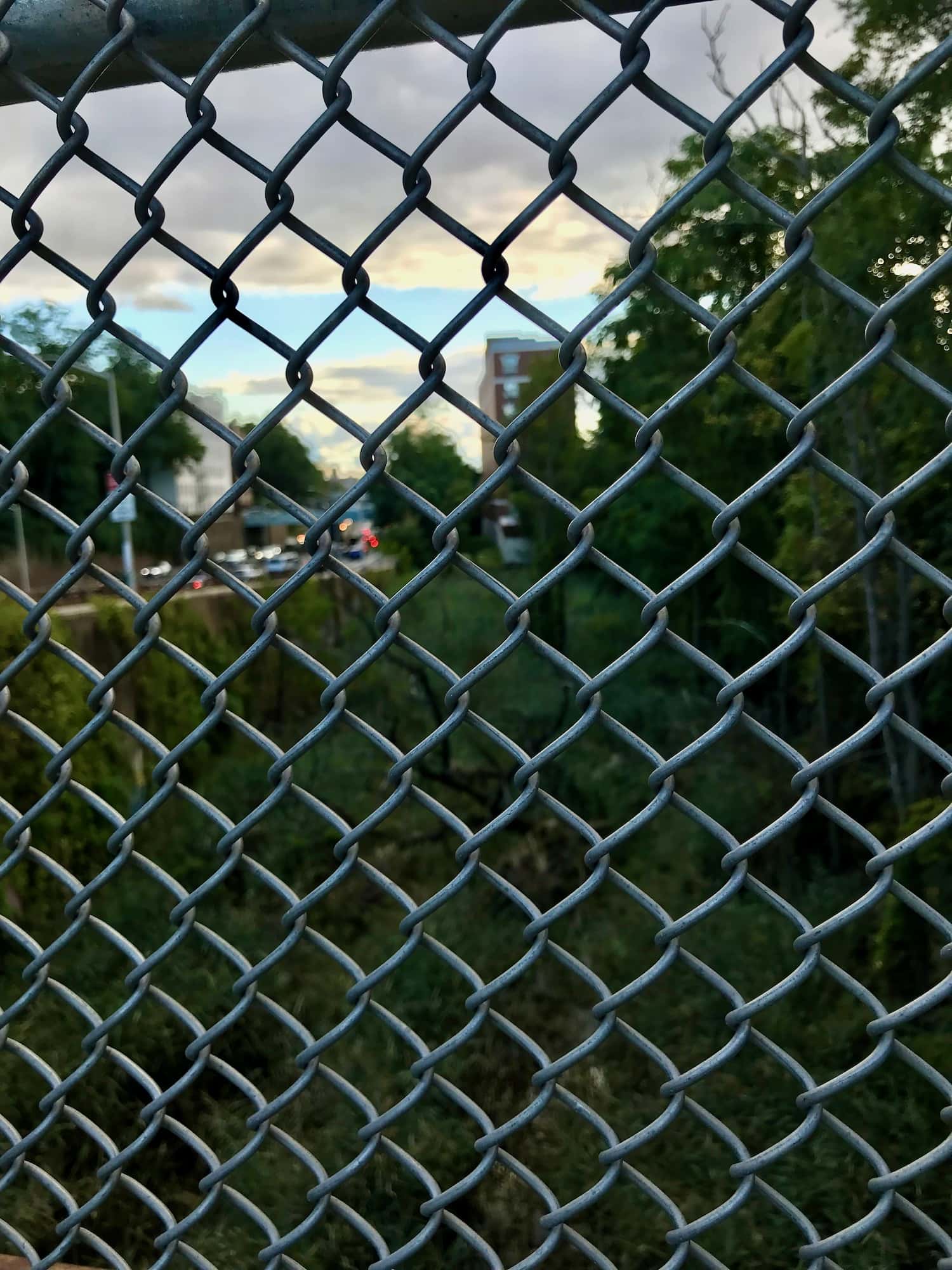 The perspective of Tibbetts Brook's potential path, framed by a chain link fence, emphasizing the separation and potential union of city and nature.