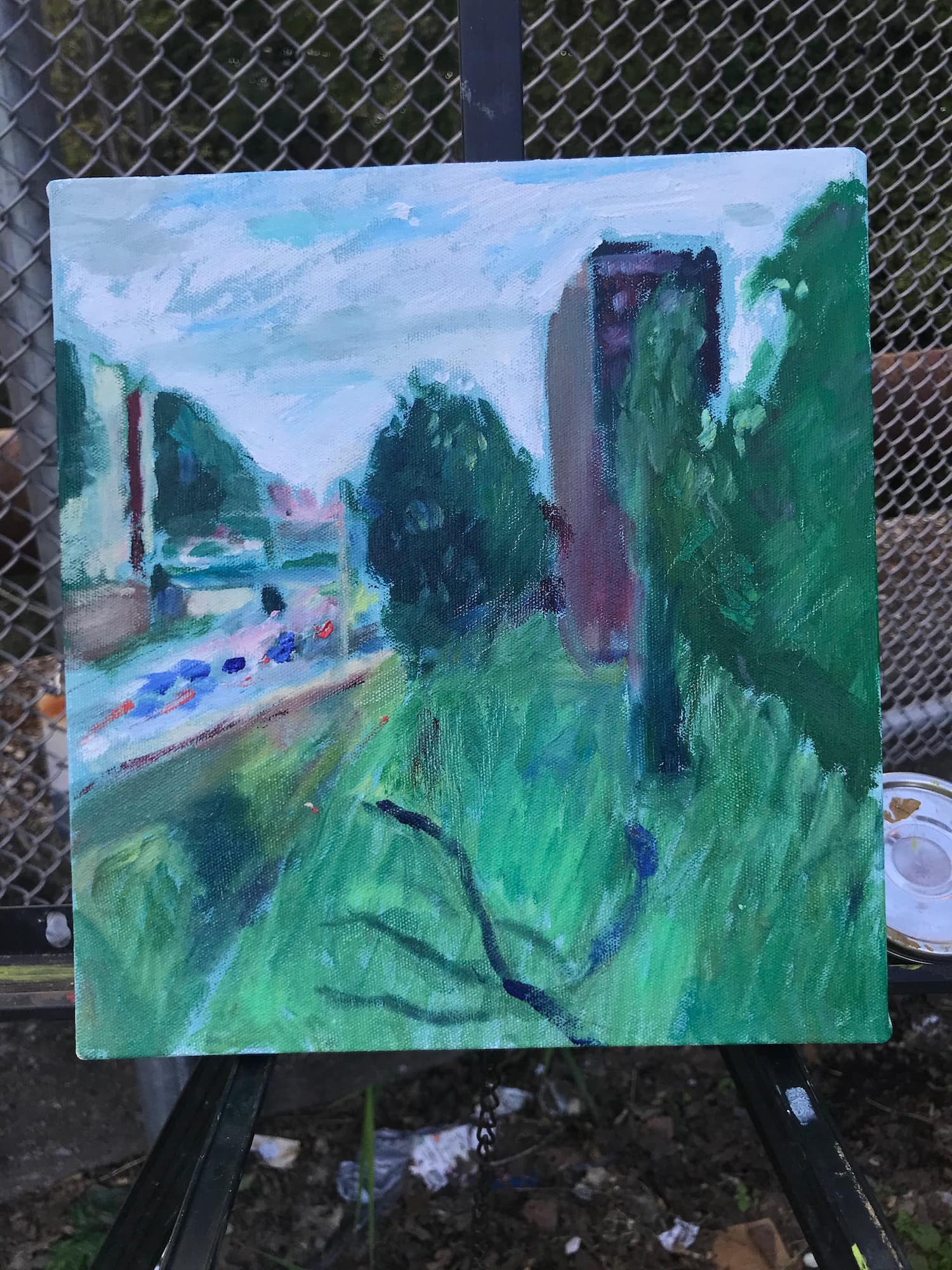 A partially completed painting on an easel depicting a green landscape with urban elements.
