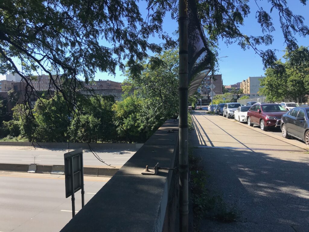 The shaded sidewalk near the Major Deegan Expressway, devoid of pedestrians.